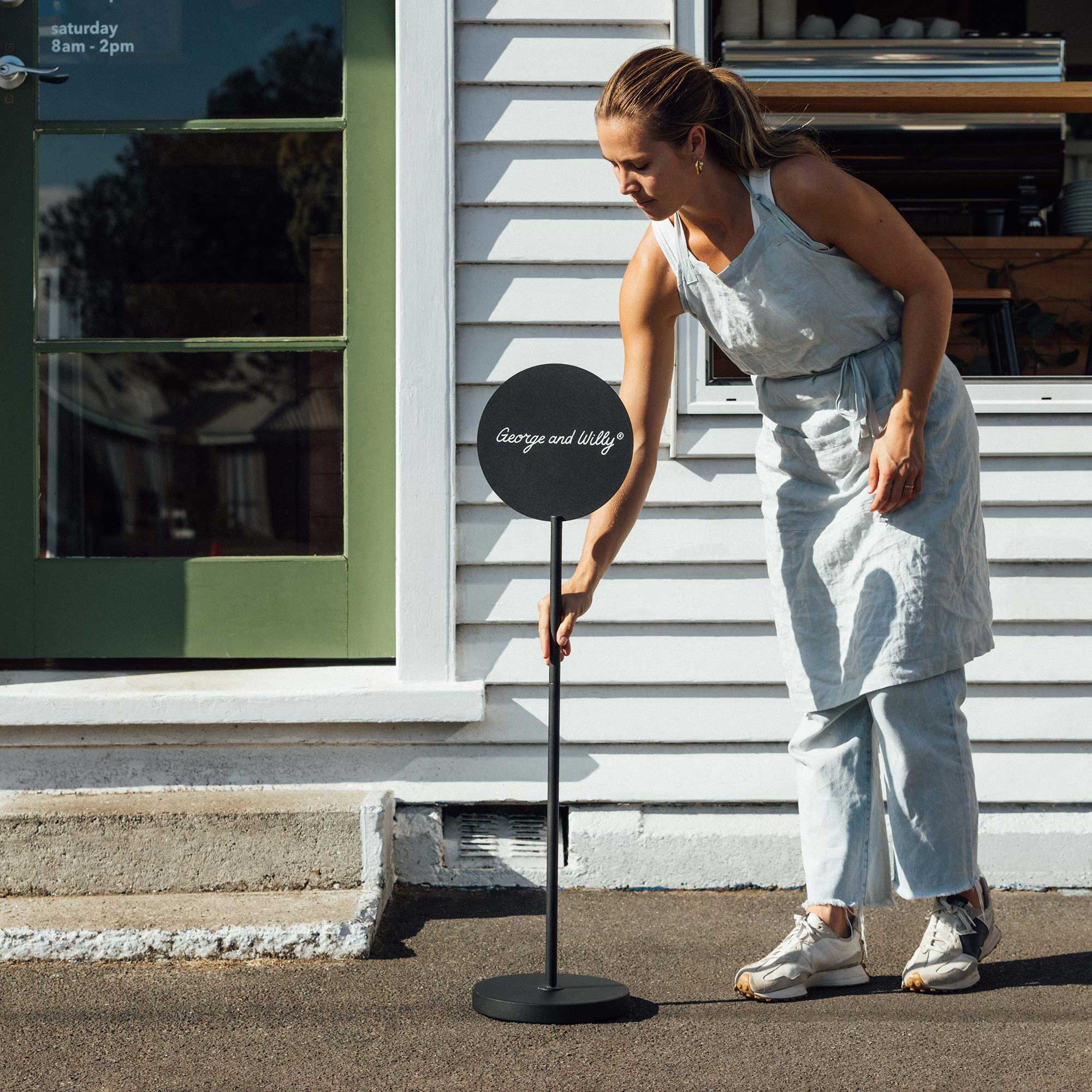 person moving a storefront black round standing lollipop sign